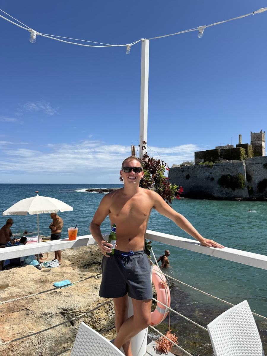 Will Tjernlund at a seaside beach club in Puglia, Italy, with a medieval fortified tower and the Adriatic Sea in the background