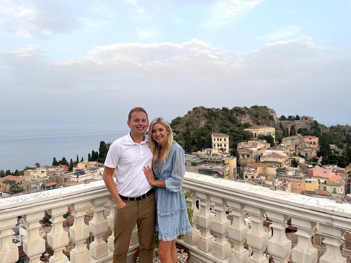 Will Tjernlund and Kelsey overlooking Taormina, Sicily from a hotel terrace with the Ionian Sea and Mount Tauro in the background